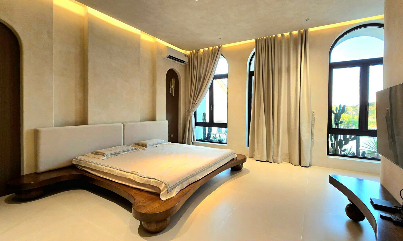 Phòng ngủ biệt thự với cửa sổ vòm cong và giường gỗ uốn lượn, thi công trọn gói